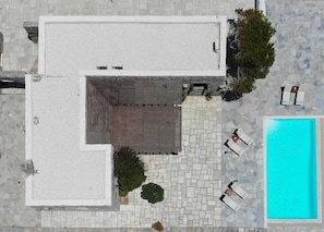 An aerial view of a building with a swimming pool, stone flooring, and outdoor seating.