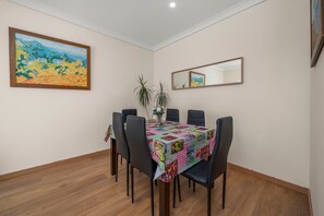 Un'area pranzo con tavolo ricoperto da una trapunta, circondato da sedie, un vaso con piante e un quadro appeso al muro.