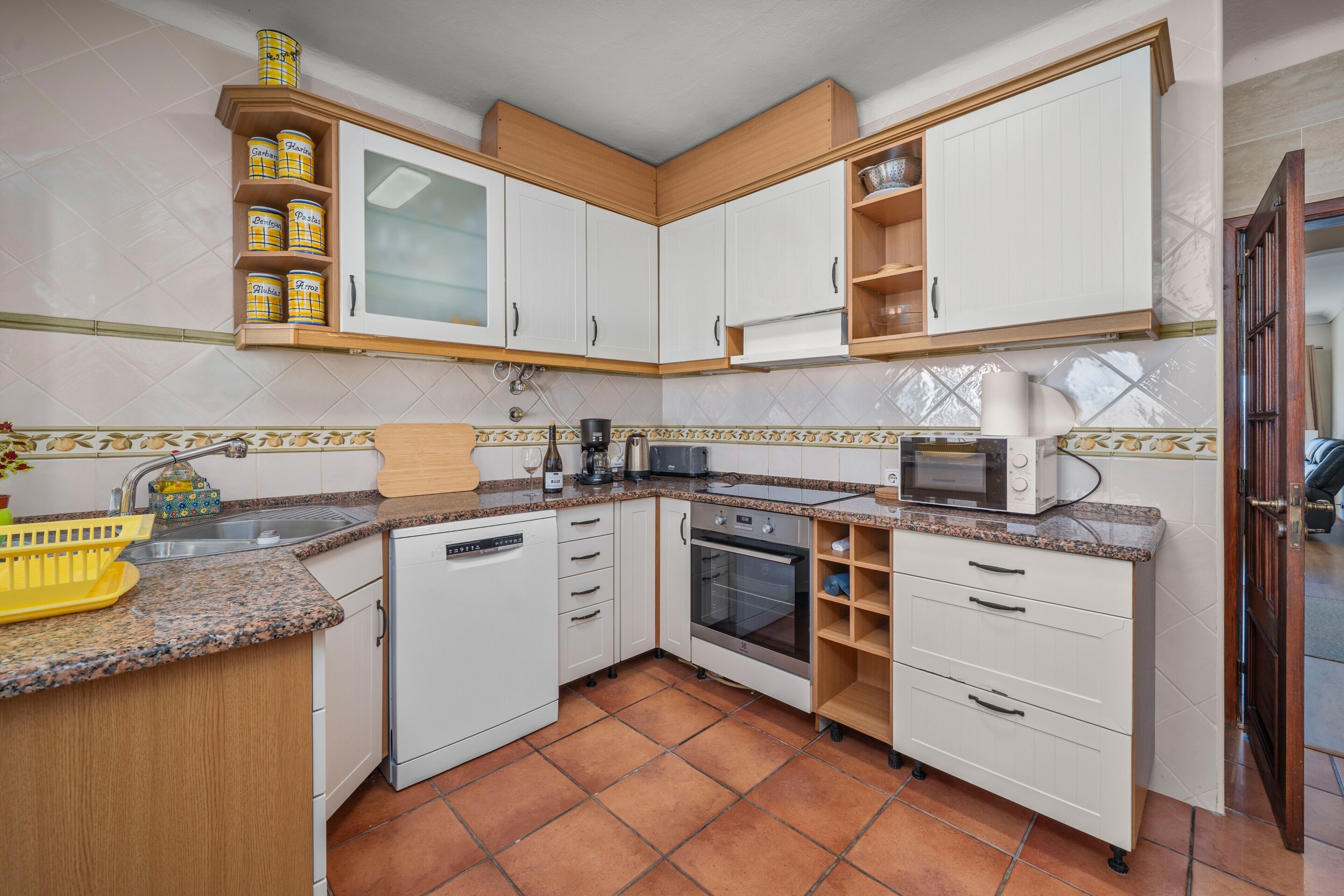 Una cocina compacta con armarios blancos, horno empotrado, microondas y pileta.