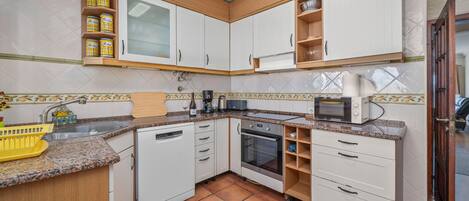 Una cocina compacta con armarios blancos, horno empotrado, microondas y pileta.