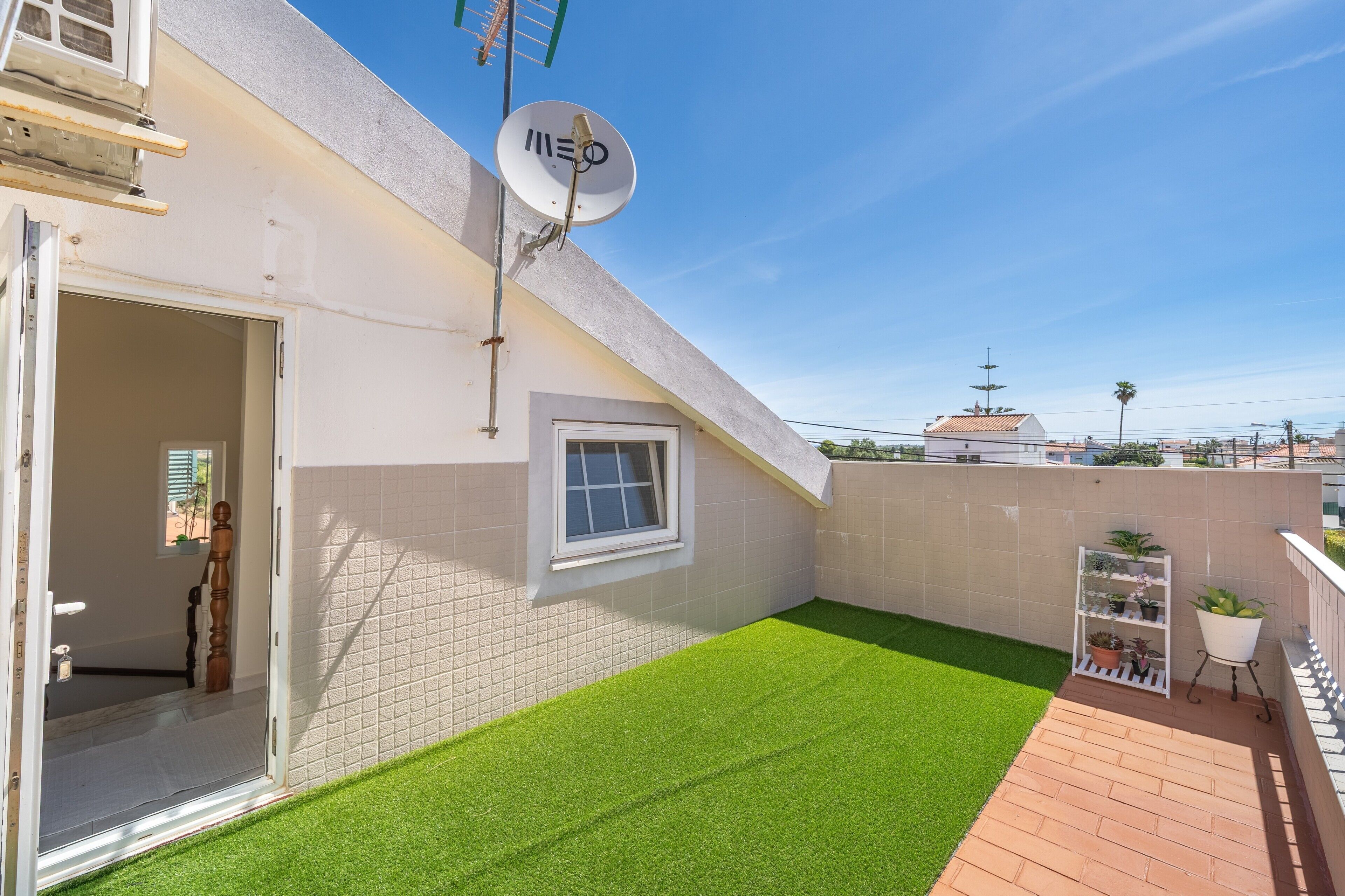 Una azotea con césped artificial, una antena parabólica, una ventana y una planta en maceta.