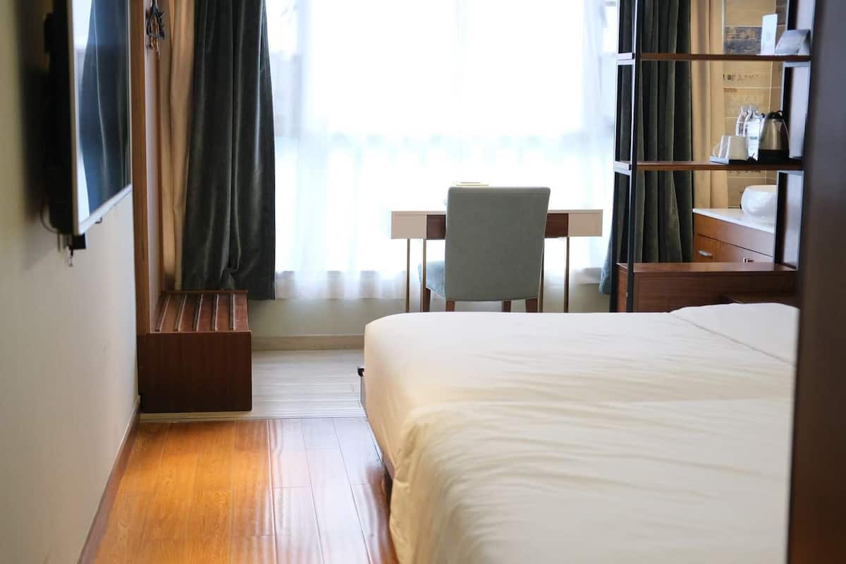 A hotel room with a bed, a desk, a chair, a TV mounted on the wall, and a bookshelf.