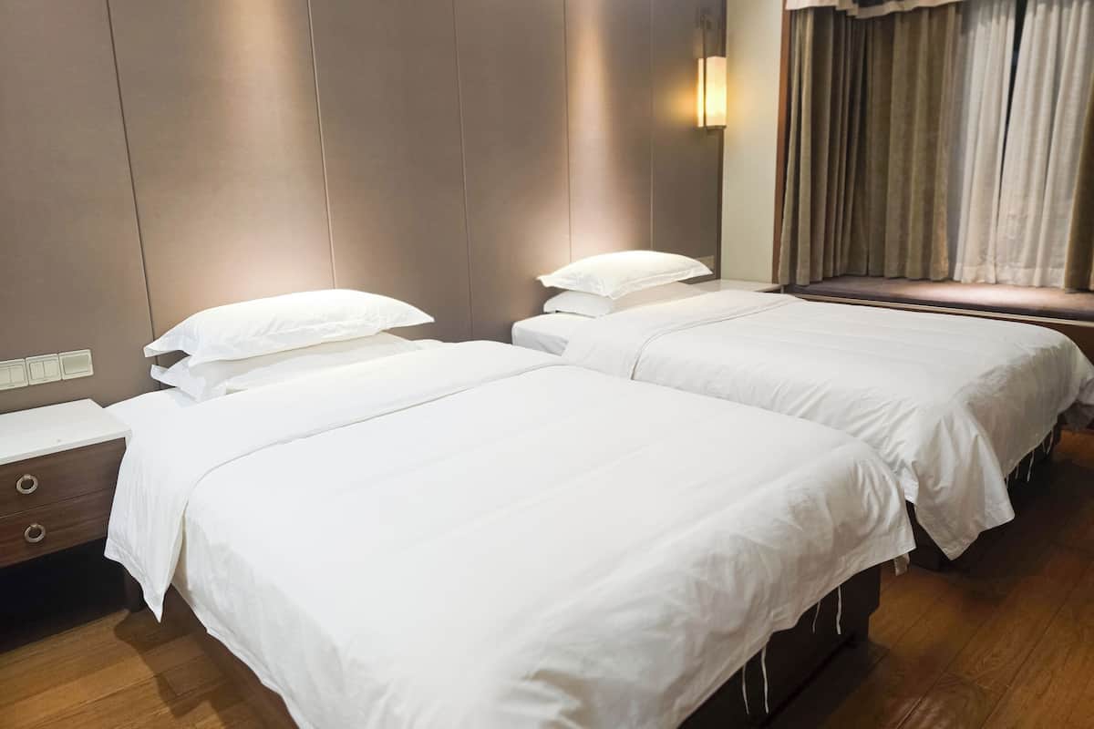 A hotel room with two beds, a nightstand, a drawer, and a window with curtains.