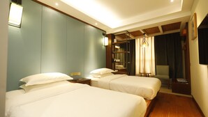 Quarto de hotel com duas camas, uma escrivaninha, uma cadeira, uma estante e um candeeiro suspenso.
