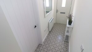 Un pasillo estrecho con baldosas de diseño, una puerta blanca, un radiador y una planta en maceta sobre un estante.