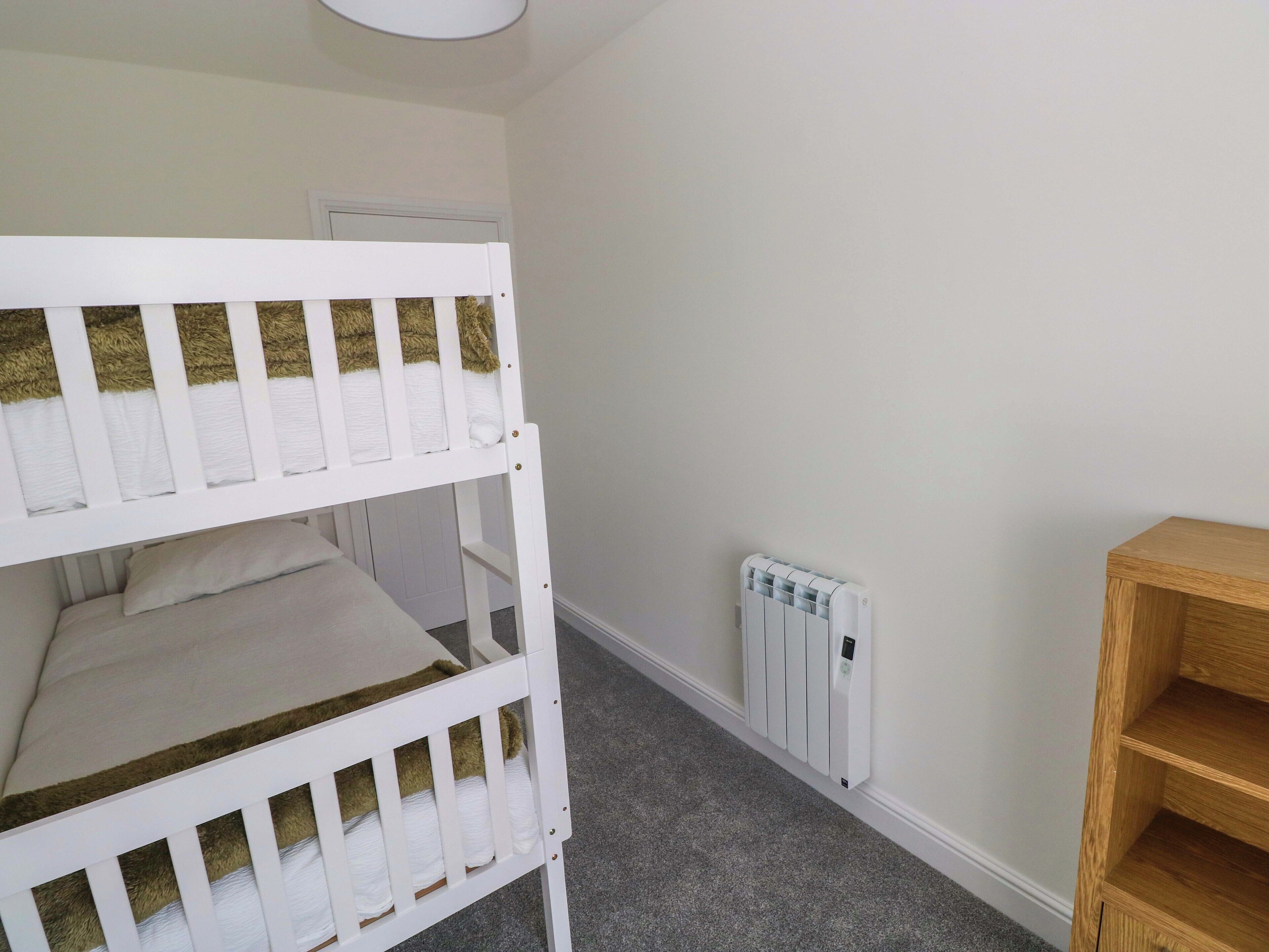 Una habitación con una cama litera, un radiador y una estantería de madera.