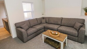 Un salón en esquina con un sofá seccional gris, una mesa de centro de madera y una ventana con persianas.