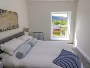 A bedroom with a bed, a radiator, a window with a view, and a painting on the wall. - Mountain View Cottage (Swansea)