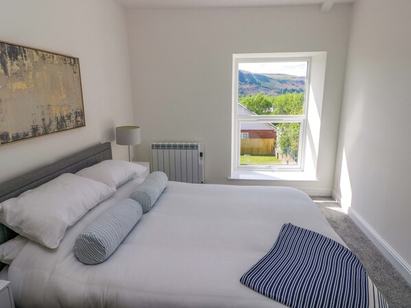 Un dormitorio con cama, radiador, ventana con vistas y un cuadro en la pared.