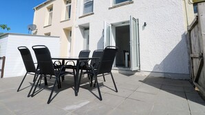 Un patio con una mesa y sillas, un edificio blanco con varias ventanas y una puerta.