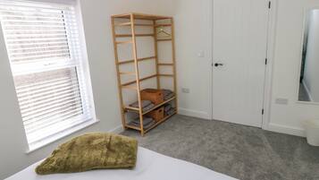 Una habitación con cama, una estantería de madera, una puerta blanca y una ventana con persianas.