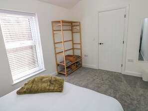 A room with a bed, a wooden shelving unit, a white door, and a window with blinds. - Mountain View Cottage (Swansea)