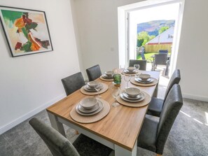 Un comedor con una mesa de madera dispuesta para cuatro personas, sillas, un cuadro en la pared y vistas al exterior a través de una puerta.