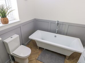 Et badeværelse med et hvidt badekar, et toilet og en lille plantepotte på vindueskarmen.
