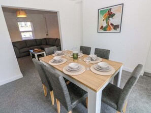 Comedor con mesa de madera dispuesta para cuatro personas, rodeado de sillas tapizadas en gris.