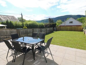 En terrasse med et bord og stole, et træhegn og en græsplæne.