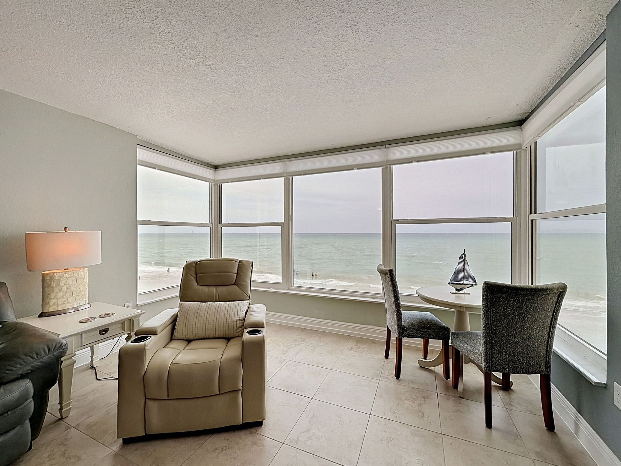A room with a large bay window, a beige sofa, a dining table with chairs, and a lamp.