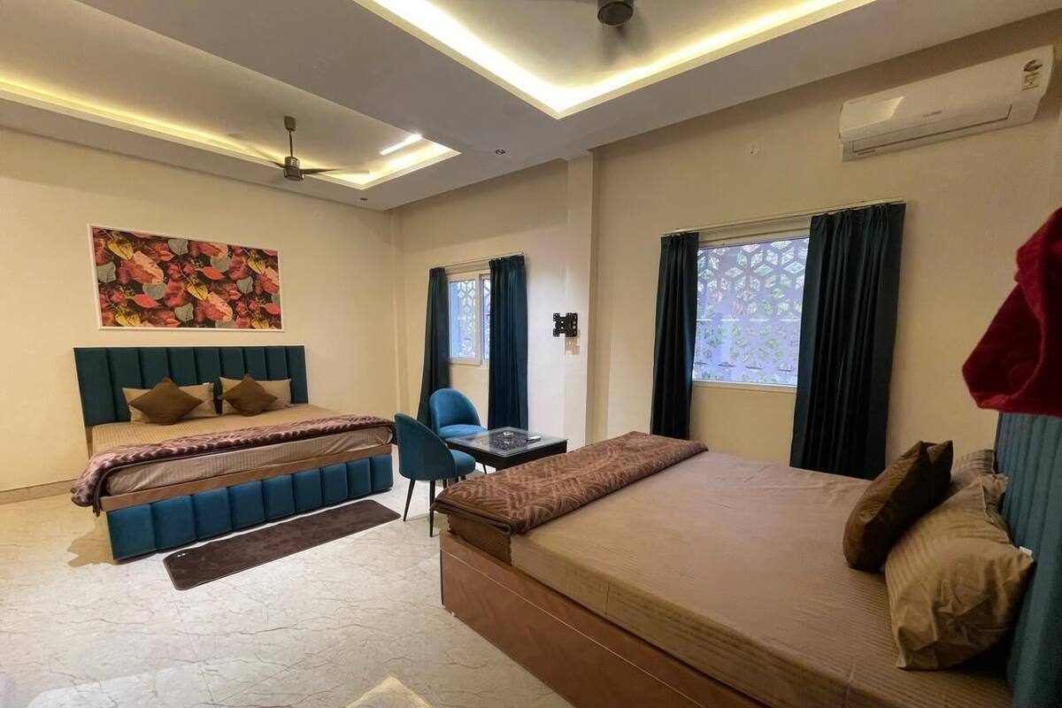 A hotel room with two beds, a desk, a chair, a ceiling fan, and an air conditioning unit.