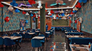 A restaurant with blue booths, tables with white tablecloths, and red, white, and blue balloons. - LIMELIGHT Hotel & Restaurant (Rishikesh)
