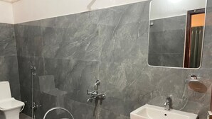 A bathroom with a toilet, a sink, a shower, and a bucket. - LIMELIGHT Hotel & Restaurant (Rishikesh)