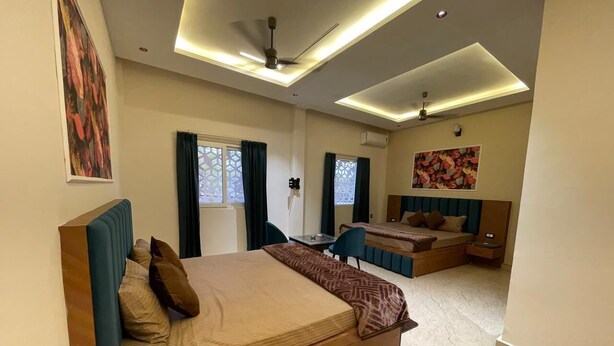 A modern bedroom with a large bed, a sofa bed, a desk, and a ceiling fan. - LIMELIGHT Hotel & Restaurant (Rishikesh)