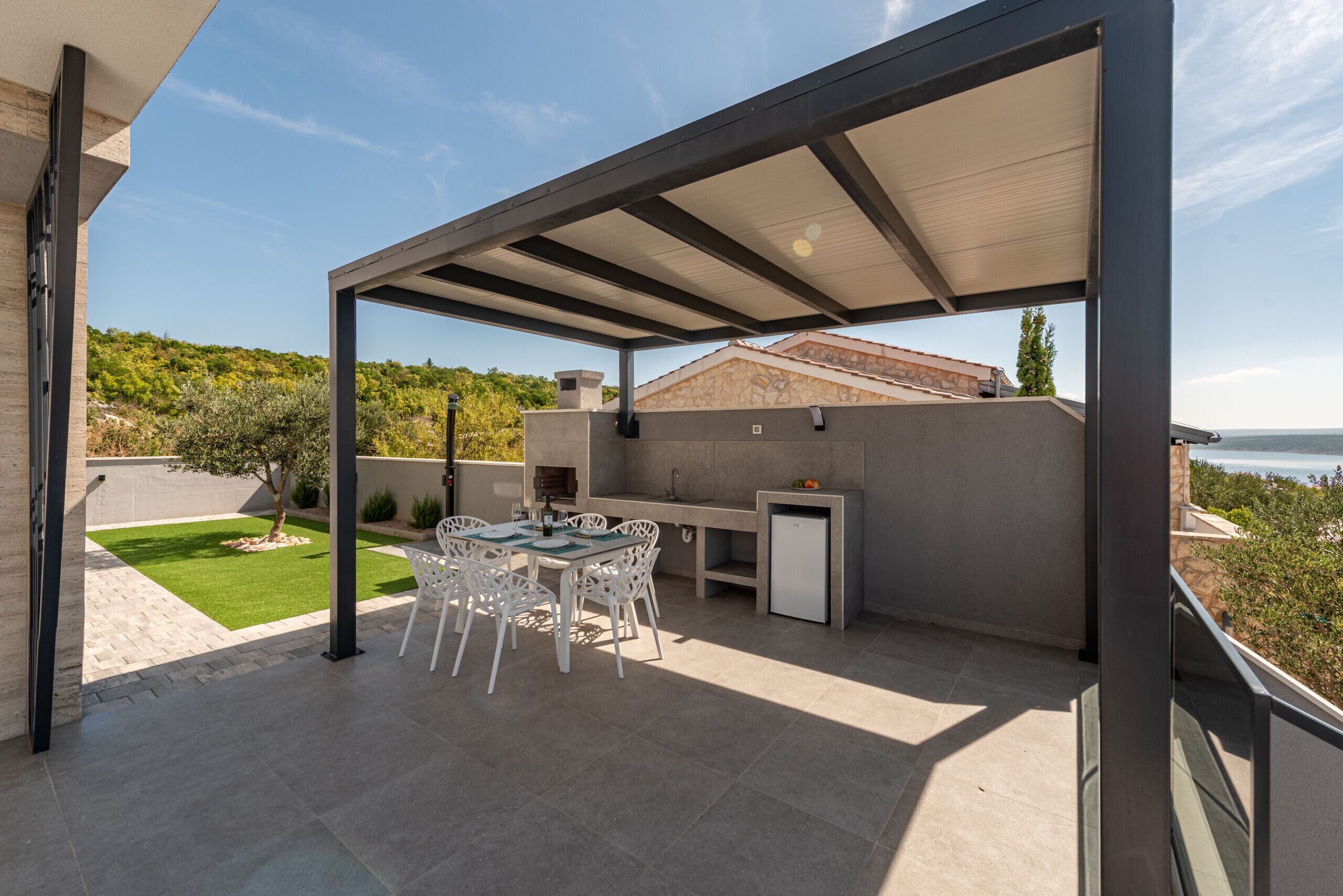Eine Terrasse im Freien mit Tisch, Stühlen, einem Grill und Blick auf das Meer.