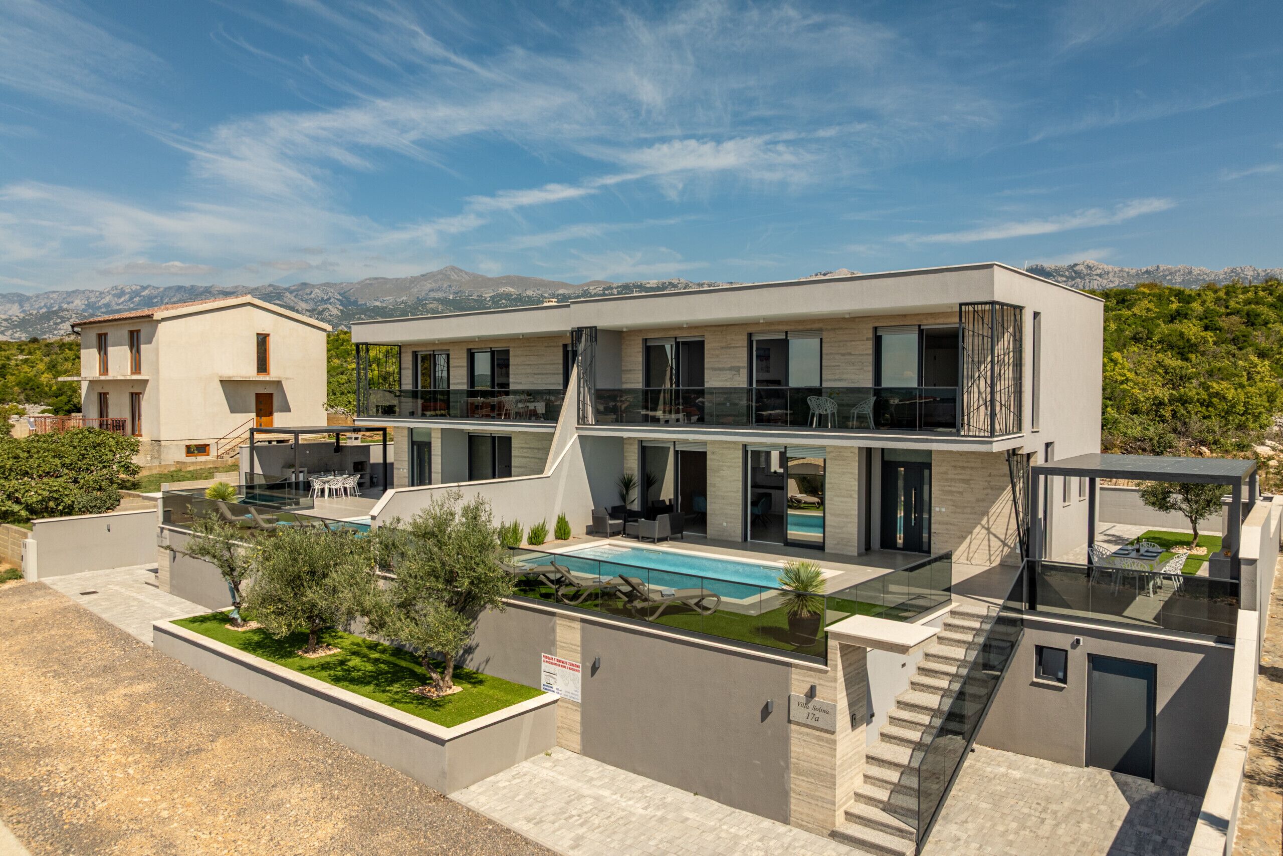 A modern two-story house with a swimming pool, outdoor seating, and a view of mountains.