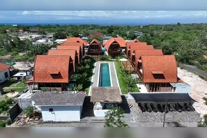 Ein Resort mit mehreren bungalowartigen Gebäuden, einem zentralen Schwimmbecken und Blick auf den Ozean.