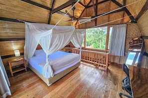 Ein Schlafzimmer einer Holzhütte mit einem Bett, einem Nachttisch, einem Schreibtisch und einem Fenster mit Vorhängen.