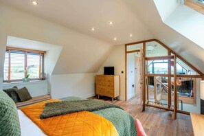 A bedroom with a bed, a dresser, a window with blinds, and a staircase leading to an upper level. - Longdale Barn (Newtown Linford)