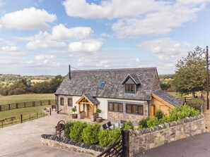 A stone house with a sloped roof, a wooden porch, and a fenced yard. - Longdale Barn (Newtown Linford)