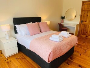 Een net opgemaakt bed met kussens, een bedlampje en een opgevouwen handdoek op een houten vloer.