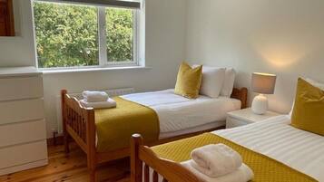 Habitación con dos camas, ventana con vista a árboles, lámpara de noche y cabecera de madera.