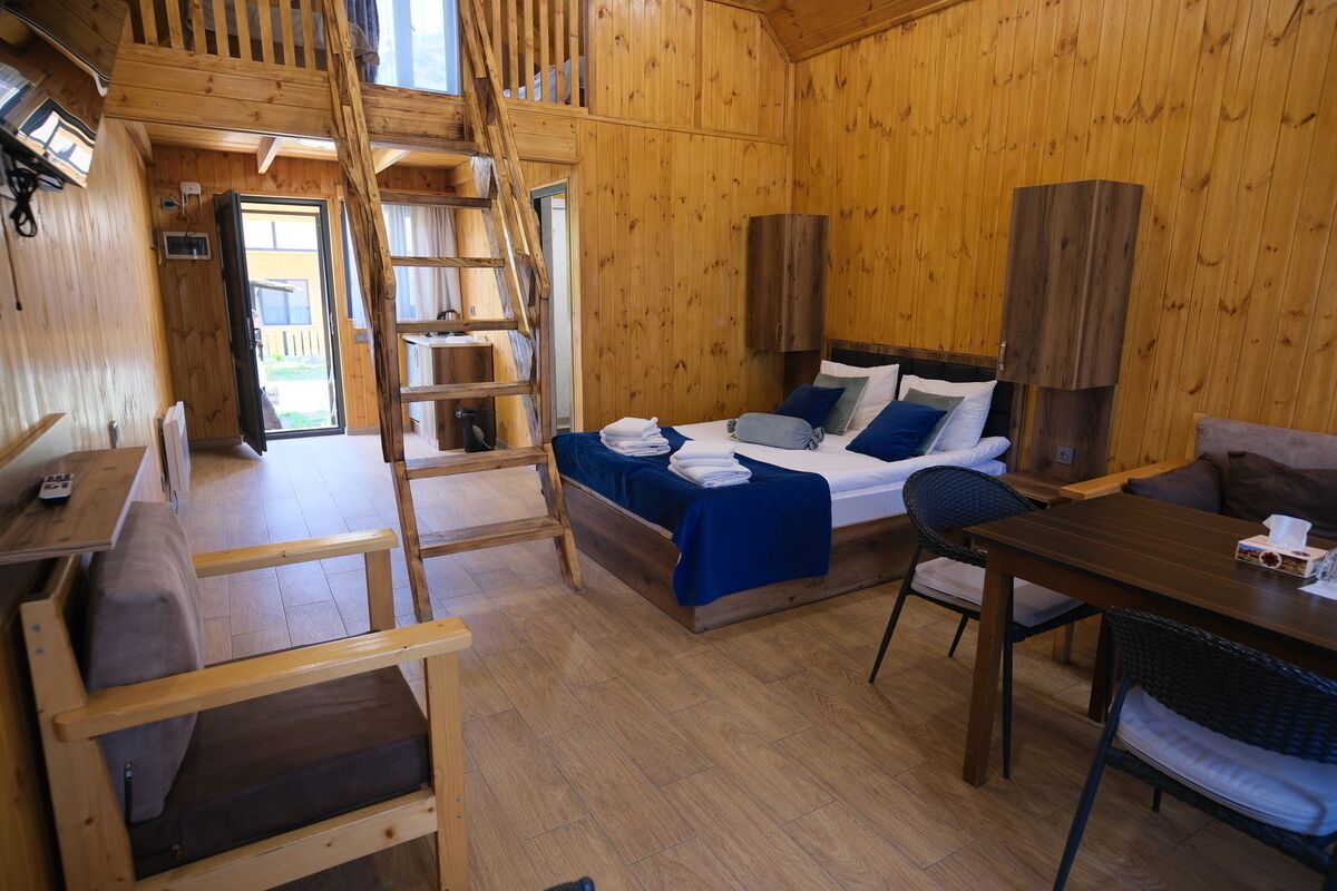 Una cabaña de madera con un dormitorio en el altillo, comedor y escalera.
