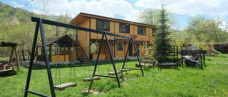 A wooden house with a swing set in a grassy yard.
