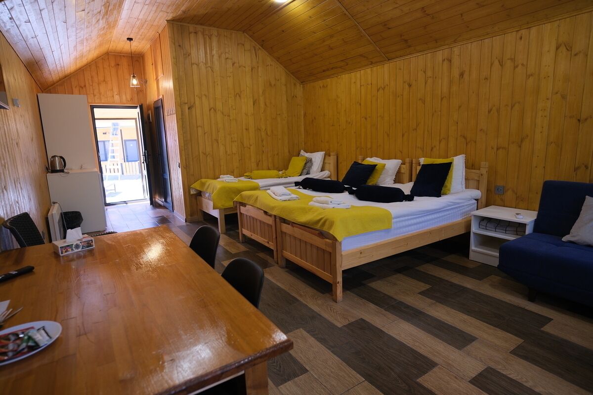 A wooden-paneled room with two beds, a table, and a sofa.