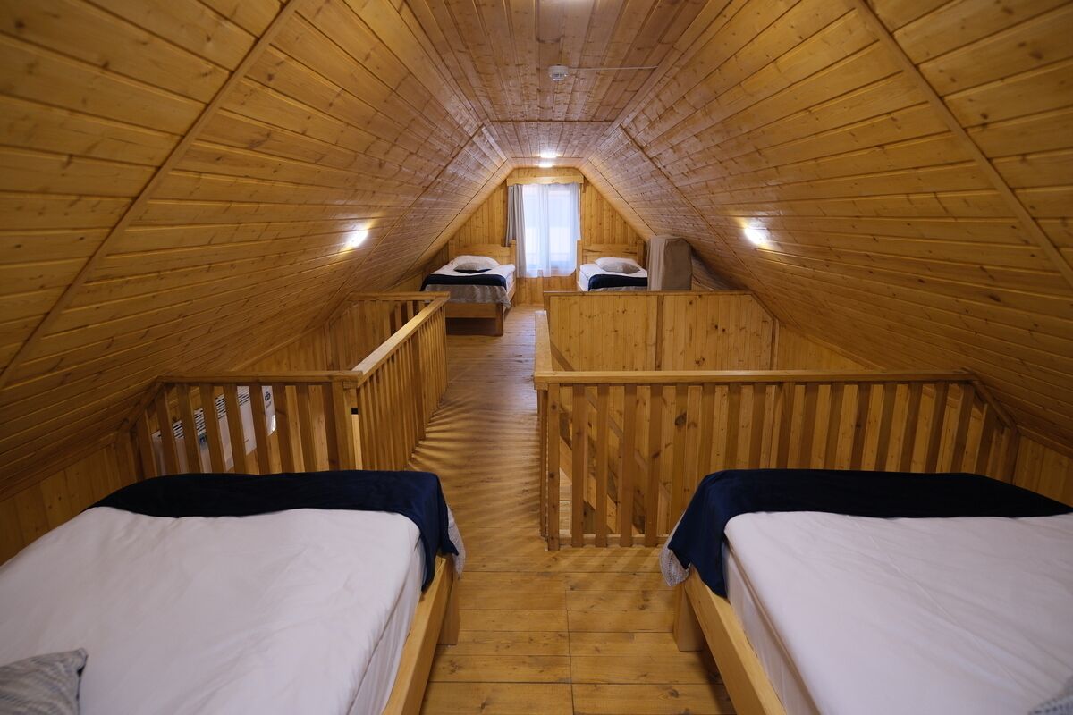 Un dormitorio de ático con piso de madera, dos camas, un ventanal pequeño y una barandilla de madera.