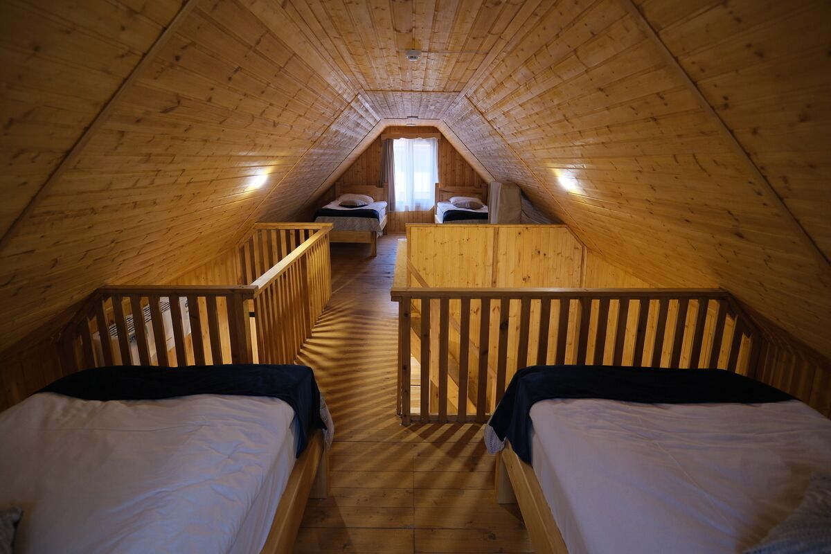 Un dormitorio en el ático con piso de madera, dos camas, una ventana y baranda de madera.