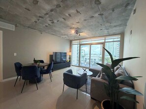 Ein modernes Wohnzimmer mit Essbereich, großen Fenstern und einer Decke mit freiliegenden Balken.