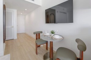A dining area with a round table, two chairs, a potted plant, and a flat-screen TV mounted on the wall. - Studio in Midtown | Standard Miami - Pool & Gym (Miami)