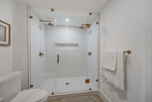 A glass-enclosed shower with a white tiled floor, a white toilet, and a towel rack with a towel. - Studio in Midtown | Standard Miami - Pool & Gym (Miami)