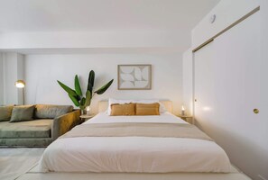 A bedroom with a bed, a sofa, a potted plant, a wall art piece, and a bedside table with a lamp. - Studio in Midtown | Standard Miami - Pool & Gym (Miami)