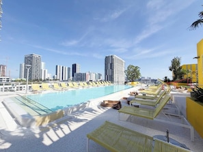 Ein Pool auf dem Dach mit Liegestühlen und einer Stadtkulisse im Hintergrund.
