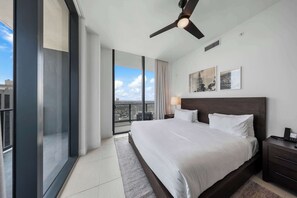 Een moderne hotelkamer met een groot bed, een plafondventilator, uitzicht op de stad en kunst aan de muur.