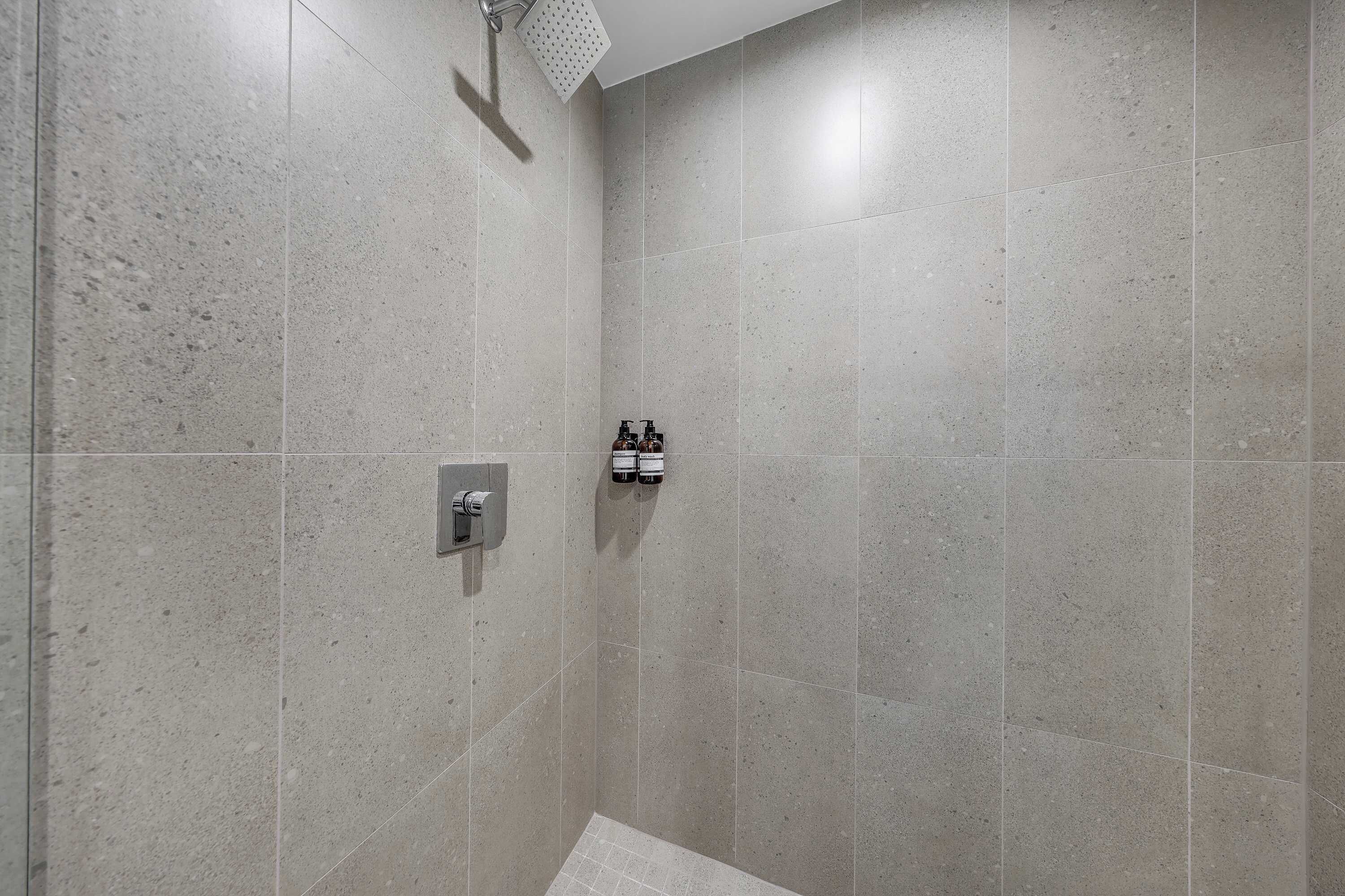 Eine Dusche mit Duschbrause, Bedienfeld an der Wand und zwei Shampoo-Flaschen.