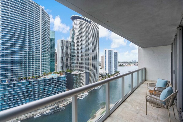 Un balcon avec vue sur des immeubles de grande hauteur, un plan d’eau et une chaise.