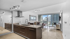 Een moderne keuken met een centraal eiland, een eethoek met een glazen tafel, en een stadszicht door grote ramen.