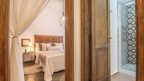 Un dormitorio con una cama, una mesita de noche, una lámpara y una puerta de madera que da a una zona de ducha.