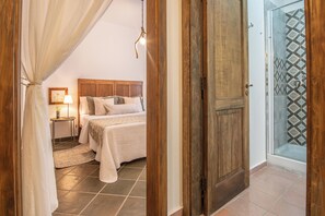 A bedroom with a bed, a nightstand, a lamp, and a wooden door leading to a shower area.