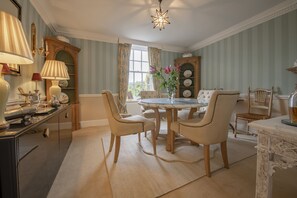 Ein Esszimmer mit einem runden Tisch, vier Stühlen, einer Blumenvase, einem Kamin und einer Deckenleuchte.
